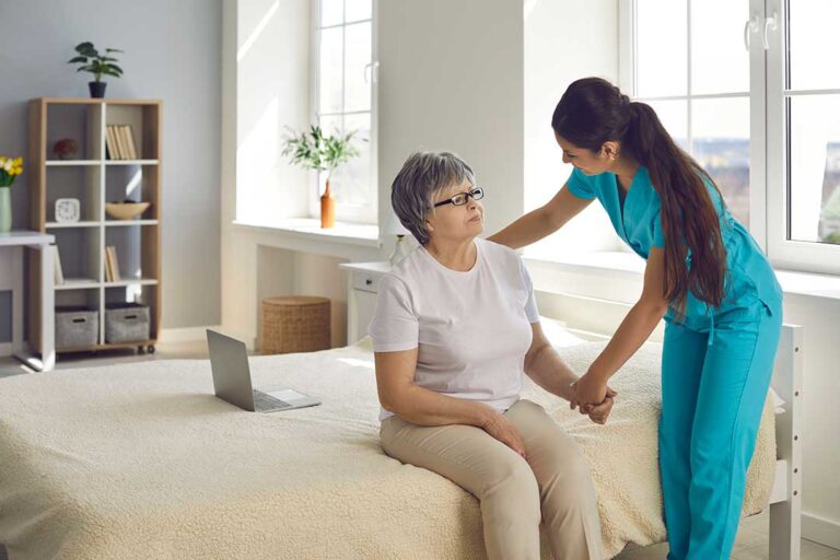 An older couple sits together in a cozy apartment, one reading while the other receives gentle assistance from a caregiver.